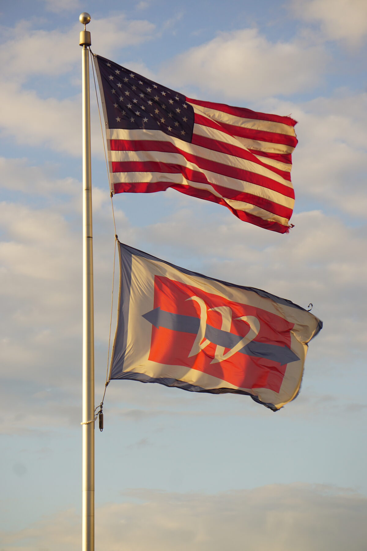 American flag flying above a second flag on a pole against a partly cloudy sky