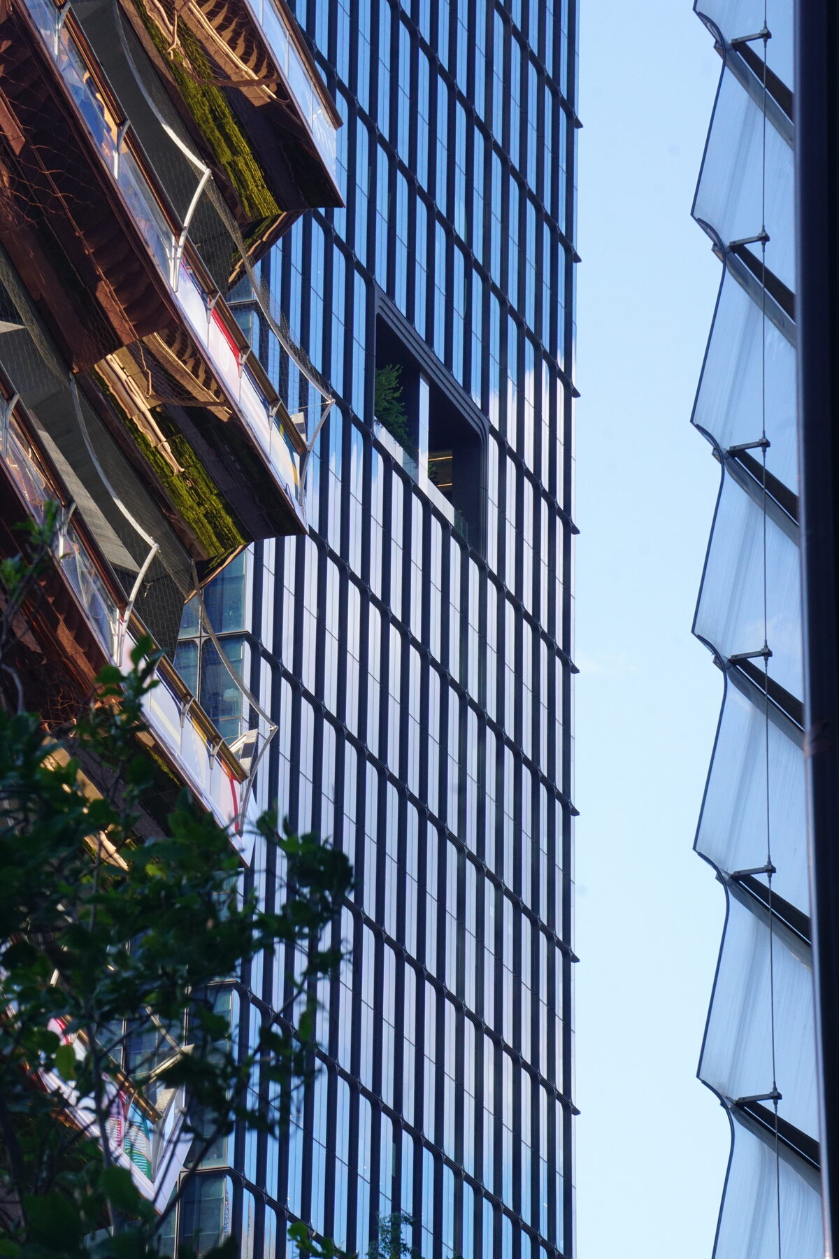 Angled view looking up at a glass skyscraper facade with greenery